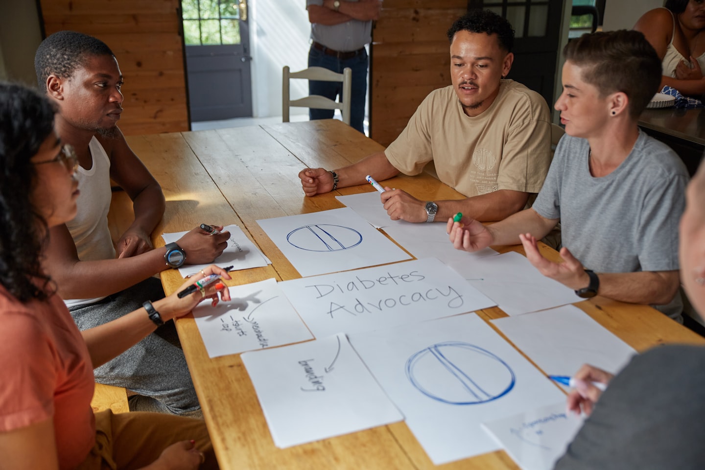 Un grupo diverso de jóvenes adultos colabora en ideas para la defensa de la diabetes en una mesa.